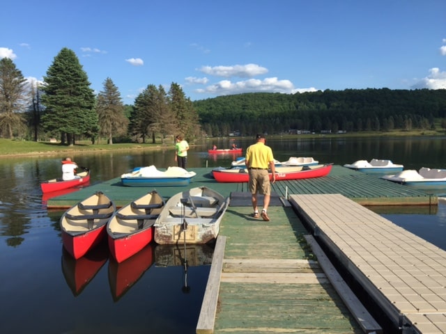A group of people standing on a dock at a campground with canoes.