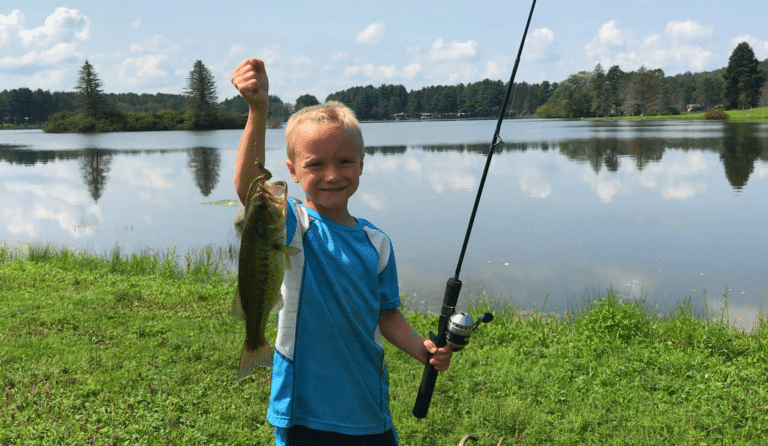 A young boy holding up a fish in front of Rainbow Lake.