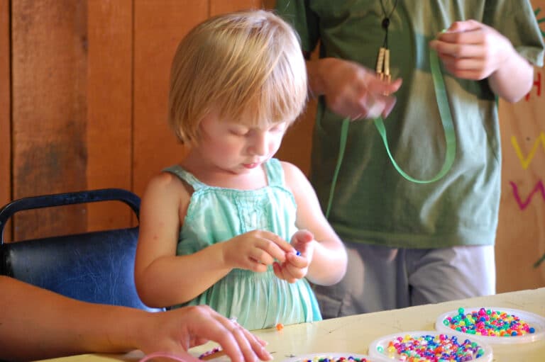 A little girl is playing with beads at a table in an RV campground.