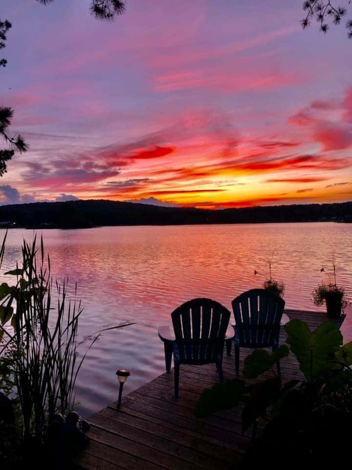 Two camping chairs on a dock overlooking Rainbow Lake at sunset in Western New York.