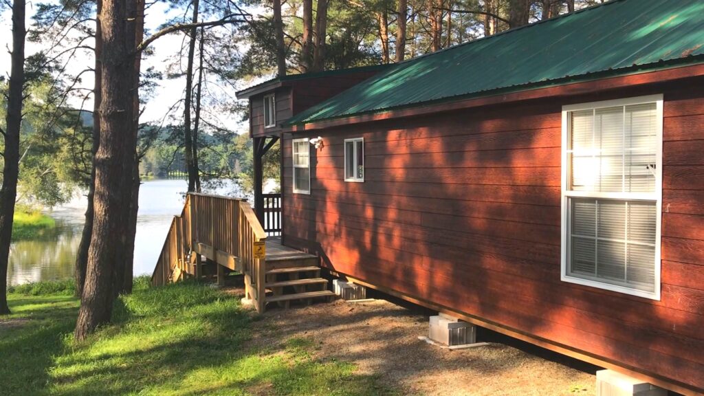 A red cabin with a green roof next to Rainbow Lake at a family campground.
