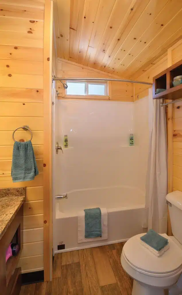 Full bathroom inside a park model cabin, with a tub and shower, granite-topped vanity and pine walls