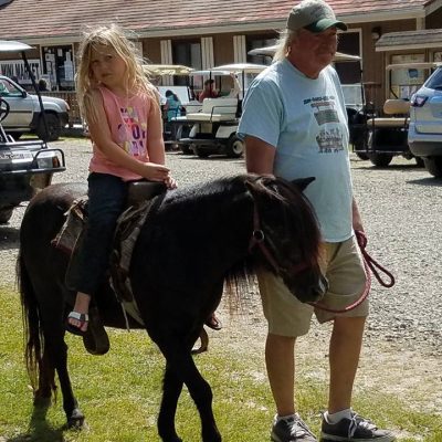 A man and a girl riding a pony in a parking lot at a western New York campground.