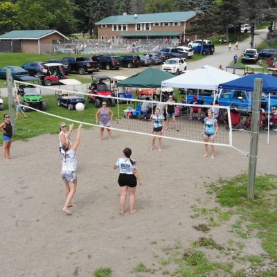 A group of people camping at an RV campground in Western New York, enjoying a friendly game of volleyball in the sand.