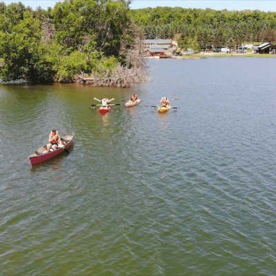 A group of people paddling in canoes on Rainbow Lake at a campground.