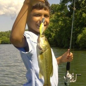A young boy holding up a large bass at a campground on the lake.