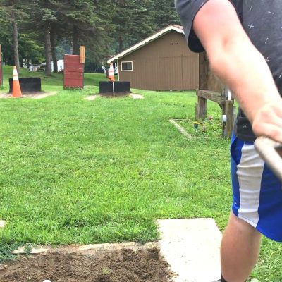 A boy is digging a hole in the ground with a shovel at an RV campground.