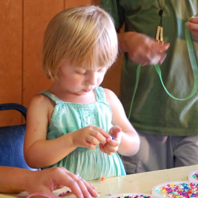 A little girl is playing with beads at a table in an RV campground.